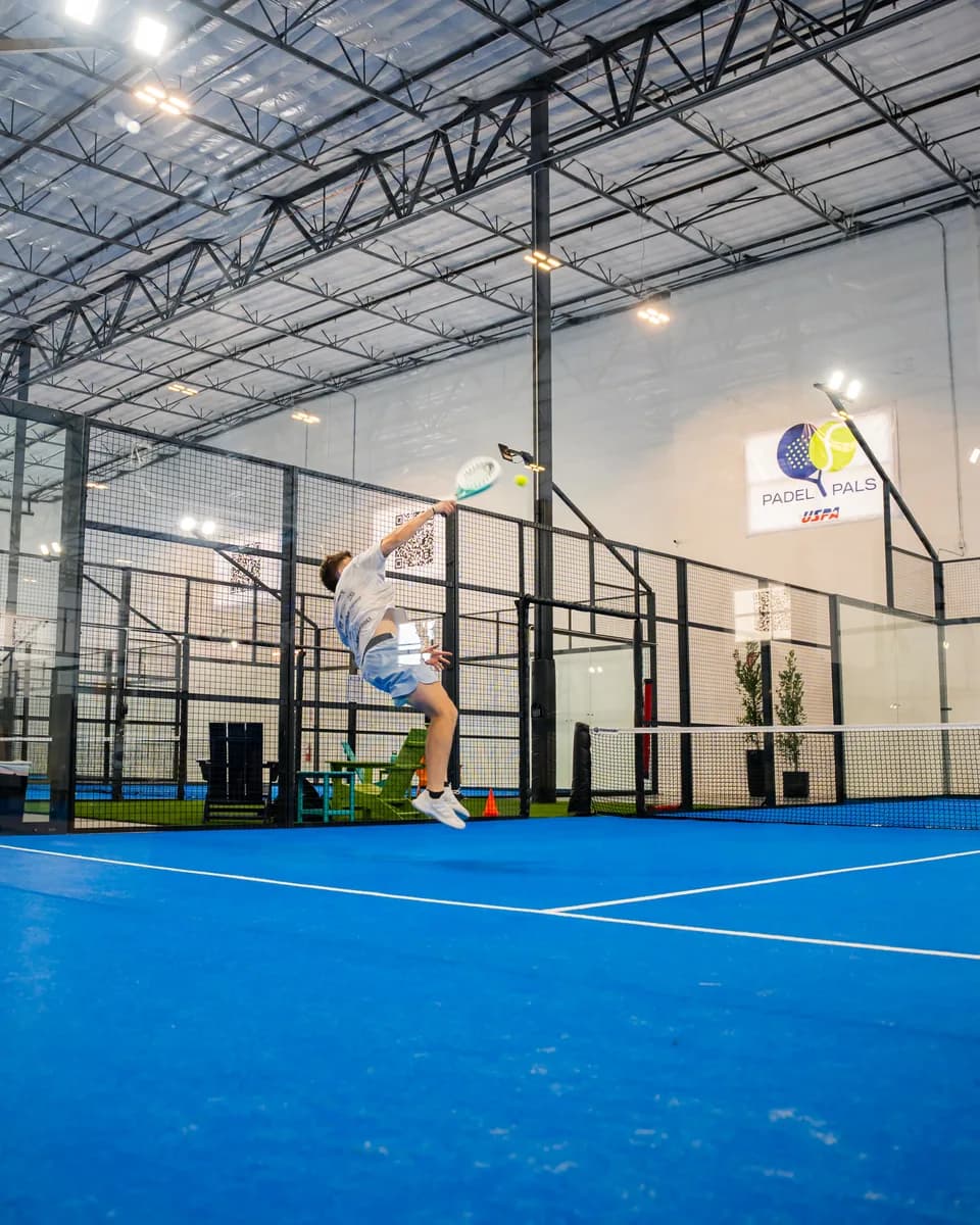 A player reaches for an overhead shot on an indoor court at Padel Pals in Mesa.